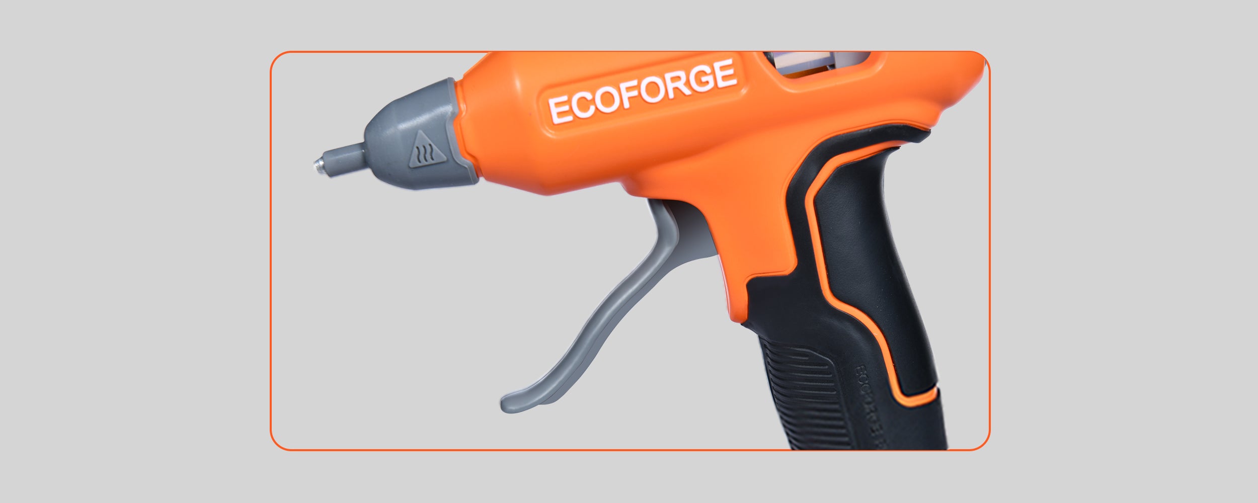 A close-up photograph of the ECOFORGE hot glue gun highlighting its extended grey trigger lever and black ergonomic grip. The matte orange housing displays the white ECOFORGE logo and a dark grey heat-resistant protective sleeve around the nozzle tip.